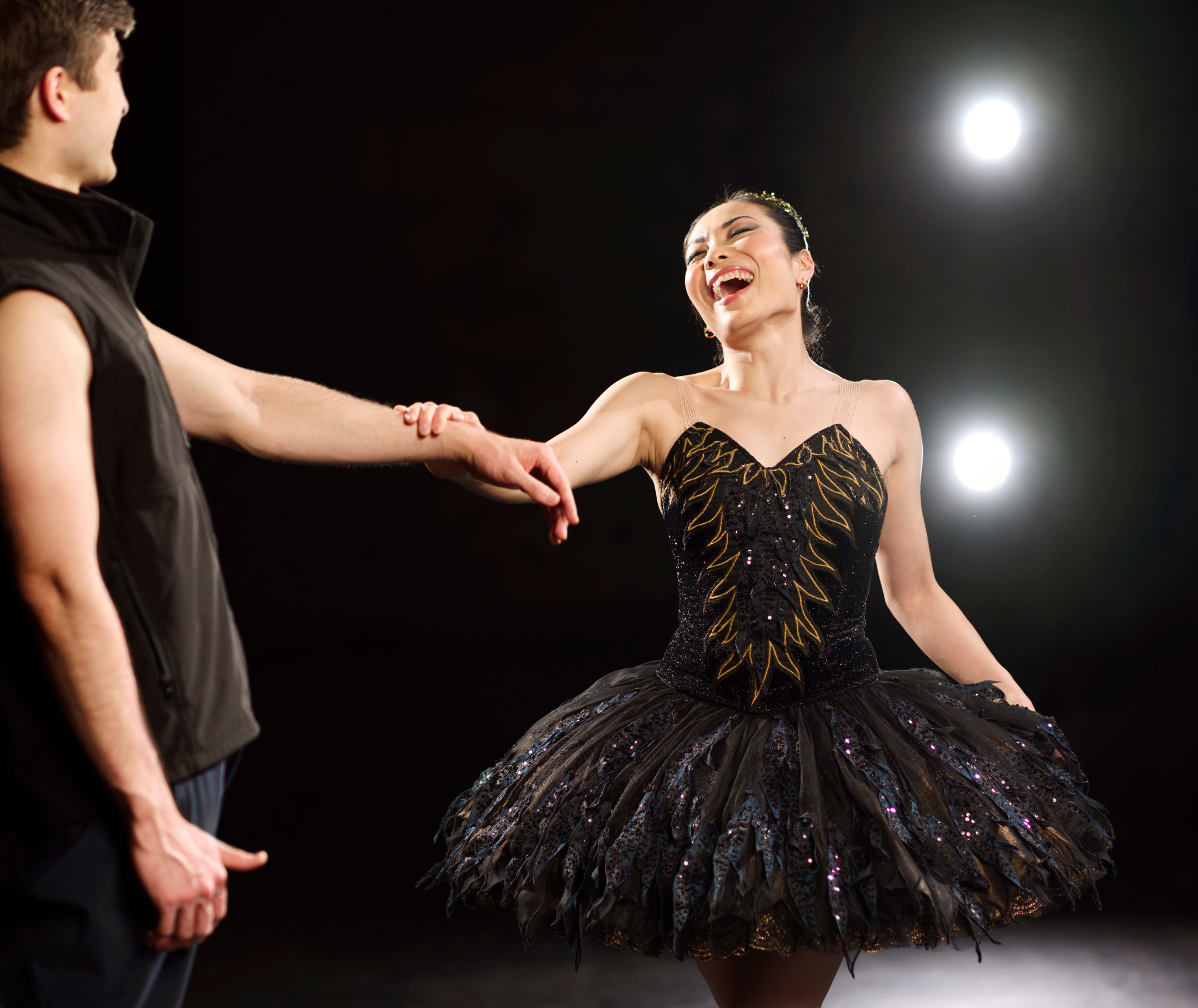Principal Mayu Tanigaito in the Black Swan tutu, wearing a tiara and pointe shoes, holding fellow Principal Laurynas Vėjalis' arm and laughing candidly